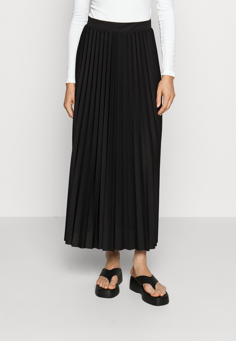 Gonna midi plissettata nera con vita elastica, realizzata in un tessuto liscio, abbinata a sandali neri con tacco a piattaforma e cinturino tra le dita.