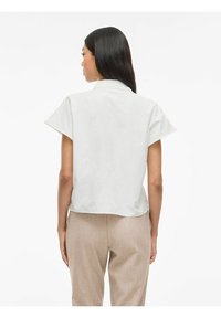 Witte blouse met korte mouwen in een ontspannen pasvorm en een omgeslagen kraag, gecombineerd met lichtbeige broek met een subtiel textuurpatroon.