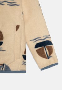 Beige fleece jacksectie met abstracte bruine en blauwe patronen, met een zijzak en grijze biezen langs de zoom en mouwen.