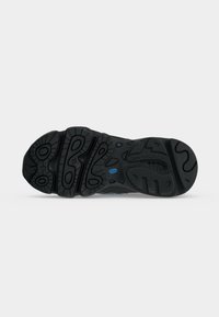 Μαύρη σόλα παπουτσιού New Balance με βαθιά αυλάκια σε κυκλικά και κυματιστά μοτίβα και ένα μικρό μπλε λογότυπο κοντά στο κέντρο.