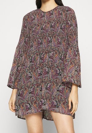 Femme portant une robe à manches longues, au-dessus du genou, avec un motif cachemire coloré et complexe dans des tons violet, orange et vert.
