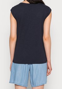 T-paita laivastonsinistä pehmeästä, kevyestä kankaasta, jossa on lyhyet hihat ja pyöreä kaula-aukko, yhdistettynä vaaleansinisiin farkkushortseihin.