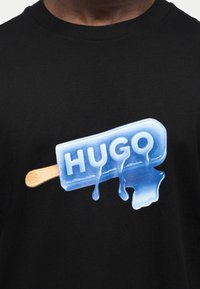 Μαύρο πουκάμισο με μπλε λιωμένο παγωτό σε γραφικό με τη λέξη «HUGO» σε ανάγλυφα γράμματα.