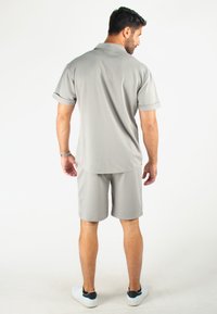 Ensemble polo gris et short en tissu léger. Comprend des manches courtes et une coupe décontractée. Chaussures blanches avec accents noirs.