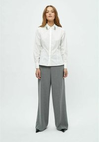 Camicia bianca con decorazioni sul colletto, abbinata a pantaloni ampi grigi chiari a vita alta.