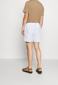 Shorts de bain rayés blancs avec une coupe décontractée, taille élastique et poches latérales, associés à un t-shirt à manches courtes marron et des sandales marron.