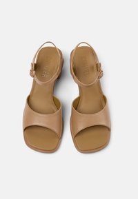 Vaaleanbeige nahkakengät, joissa on neliömäinen kärki, säädettävä hihna, tasapohja ja sileä pinta. Brändäys näkyy pohjallisesti.