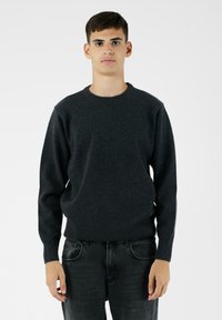 Ciemnoszary sweter dzianinowy z okrągłym dekoltem, długimi rękawami i prążkowanymi mankietami. Noszony z ciemnymi dżinsami, na jednolitym białym tle.