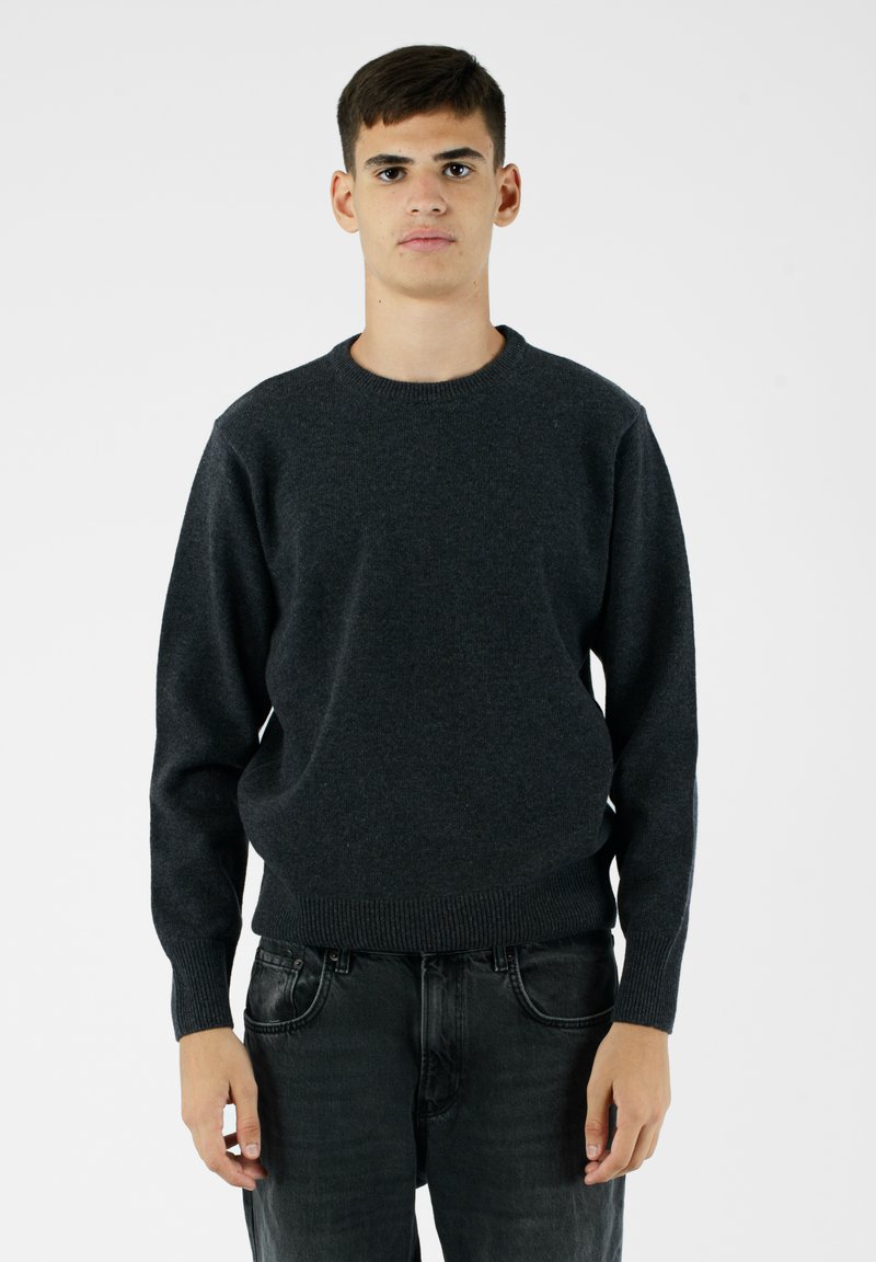 Ciemnoszary sweter dzianinowy z okrągłym dekoltem, długimi rękawami i prążkowanymi mankietami. Noszony z ciemnymi dżinsami, na jednolitym białym tle.