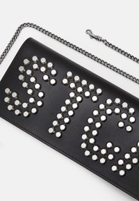 Svart läderkuvert med silverfärgade metallnitar som bildar bokstäver, med en avtagbar silverkedjesnor och en slät yta.