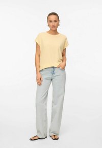 Geel gestreept T-shirt met korte mouwen en een relaxte pasvorm, gecombineerd met lichtblauwe wijde jeans en zwarte teenslippers. Simpele en casual stijl.