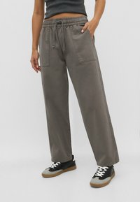 Henkilö, joka on pukeutunut avariin harmaisiin housuihin, joissa on nyöri vyötäröllä ja läpivientitaskut, sekä mustiin ja harmaisiin lenkkareihin, joissa on valkoiset nauhat.