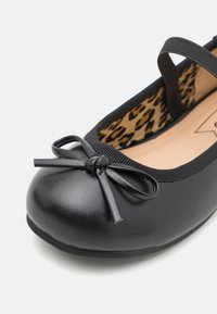 Bailarina negra con parte superior sintética lisa, con detalle de lazo en la puntera y forro de estampado de leopardo. Incluye una correa delgada para el tobillo.