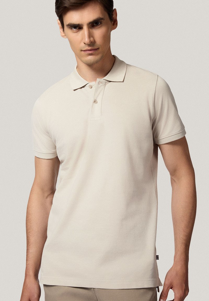 Beżowa koszulka polo wykonana z bawełny, z klasycznym kołnierzykiem, zapięciem na trzy guziki, krótkimi rękawami i subtelną teksturą.
