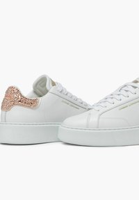 Sneaker bianche in pelle con un accento in oro rosa texture sul tallone, lacci bianchi e una suola bianca spessa. Sul lato presenta un logo.