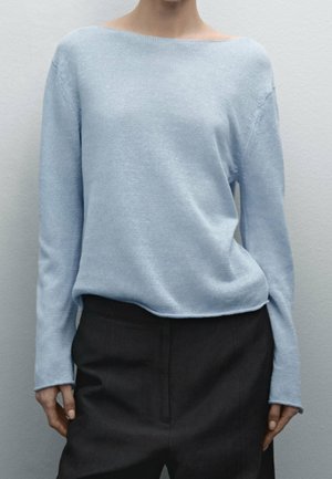 Person wearing a light blue boat neck sweater with long sleeves and black high-waisted pants against a plain light gray background.