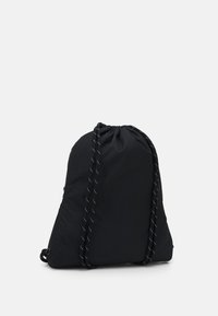 Bolsa de cuerda negra hecha de un material suave y liviano, con costuras blancas contrastantes en las correas y una forma triangular simple.