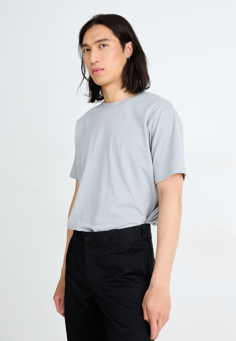 Hellgraues Baumwoll-T-Shirt mit kurzen Ärmeln und rundem Halsausschnitt, kombiniert mit schwarzen Hosen mit Knopfverschluss und Seitentaschen.