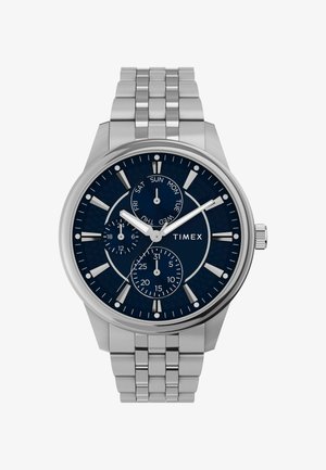 Timex horloge met een roestvrijstalen band, marineblauwe wijzerplaat, drie sub-dials voor dag, datum en 24-uurs tijd, met zilveren uurmarkeringen.