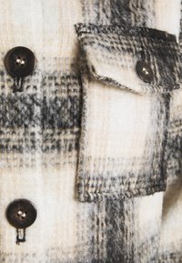 Buffalo check flannel jacket in white and black. Features dark buttons, a chest pocket, and a soft texture with a woven pattern.