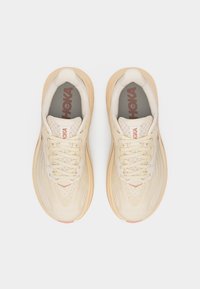 Par beige Hoka løpesko med lisser, mesh-overdel og behagelige såler, sett ovenfra på hvit bakgrunn.