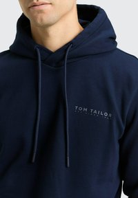 Marineblauer Kapuzenpullover aus weichem Stoff. Mit vorderseitigem Logodruck und verstellbaren Kordeln an der Kapuze.