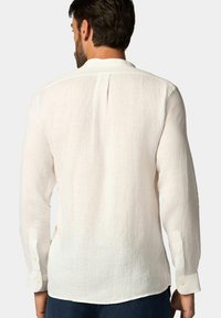 Camicia bianca in lino a maniche lunghe con piega sul retro, orlo arrotondato e polsini con bottone, che mette in mostra un tessuto rilassato e dalla texture interessante.