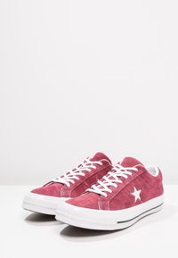 Red suede sneakers with white laces and a white star accent. Features a rubber sole and a textured upper. Classic low-top design.