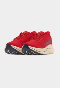 Ζευγάρι κόκκινων παπουτσιών HOKA για τρέξιμο με μπεζ ενδιάμεσα πέλματα και μαύρες εξωτερικές σόλες, σε θέα από μπροστά σε λευκό φόντο.