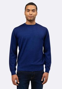 Maglione blu navy a girocollo realizzato in materiale morbido, con maniche lunghe e polsini a costine. Indossato con jeans scuri.