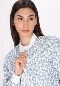 Giacca bomber azzurro chiaro con un motivo a stampa leopardata in blu scuro, con colletto e polsini a coste bianchi, e una chiusura frontale con zip.