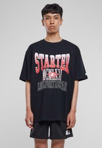 Juodas didelis T-shirt su ryškiomis raudonomis ir baltomis grafikos užrašais "STARTER" ir "LOOK FOR THE STAR", trumpomis rankovėmis ir apvalia iškirpte.