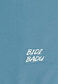 Tejido azul claro con una textura suave, con un logotipo blanco "BIDI BADU" en una fuente juguetona y negrita.