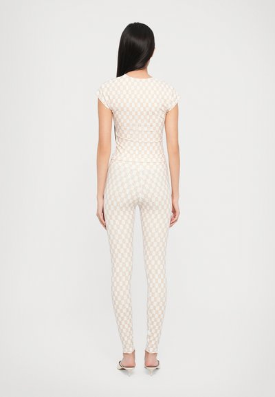 Vit fitted topp och leggings med ett subtilt geometriskt mönster i ljus orange. Materialet har en mjuk, elastisk textur. Ingen synlig hårdvara.