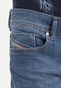 Pantalones vaqueros de mezclilla azul con un corte clásico, costuras prominentes, bolsillos laterales y traseros, y una etiqueta de marca visible en el bolsillo trasero.