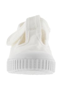 Witte canvas sneakers met een rubberen zool, voorzien van een klittenbandsluiting, een gladde textuur en een rond neusontwerp. De onderkant heeft een geribbeld patroon.