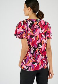 Top de manga corta con una base negra y vibrantes estampados de hojas en rosa, morado y naranja. La tela tiene una textura suave y mangas con volante.