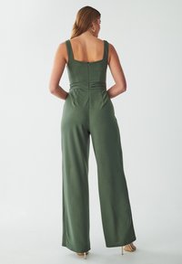 Groene jumpsuit met brede benen, aansluitend lijfje, vierkante rug en geplooid taille-detail. Gemaakt van zachte, gladde stof.