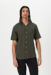 Camisa de manga corta de color verde oliva, con cuello, hecha de tejido ligero, que presenta un cierre de botones en la parte delantera y un corte relajado.