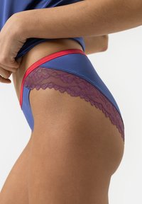 Hipster underwear in blue fabric with red accents, featuring a lace trim in purple. Smooth texture with floral lace detailing.
