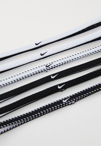Nike elastične trake u crnoj i bijeloj boji. Značajke uključuju rebrastu teksturu, različite širine i prepoznatljivi logotip otisnut duž cijele dužine.