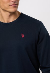 Marineblå langermet skjorte laget av bomull, med ribbestruktur og en liten rød brodert logo på venstre bryst.
