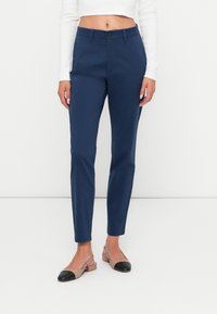 Marineblå skreddersydde bukser med slim passform, med knappeåpning og flat front. Kombinert med beige slingback sko med svarte detaljer.