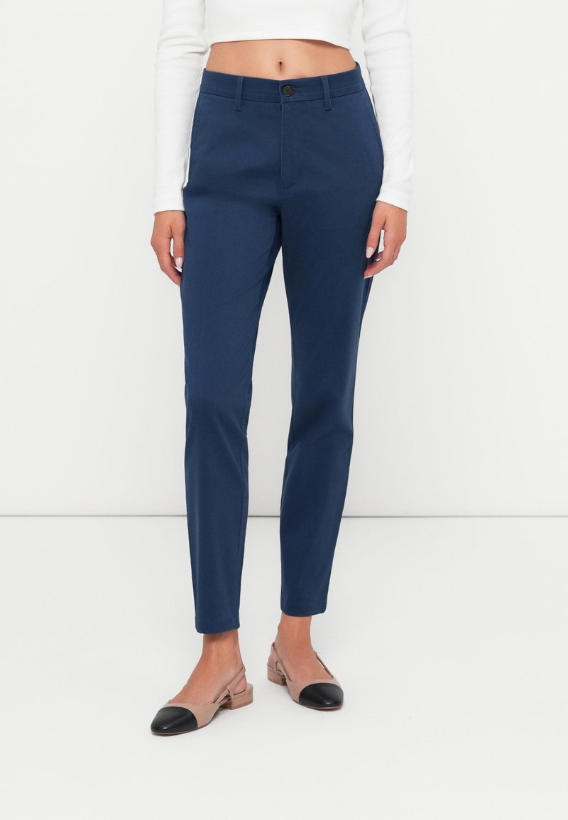 Marineblå skreddersydde bukser med slim passform, med knappeåpning og flat front. Kombinert med beige slingback sko med svarte detaljer.