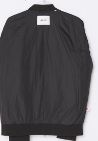 Sort bomberjakke med en glat tekstur, ribbede manchetter og en bagpå etikette med teksten "NN. 07." Har en hængende løkke ved kraven.