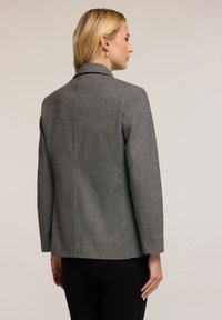 Blazer grigio a spina di pesce con colletto a punta, maniche lunghe e silhouette strutturata. Il retro presenta dettagli delle cuciture sottili e una superficie liscia.