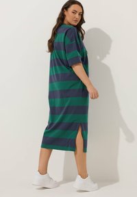 Raidallinen, polvimittainen mekko vihreästä ja laivastonsinisestä puuvillasta, jossa on lyhyet hihat, sivuhalkiot ja rento malli. Yhdistetty valkoisiin lenkkareihin.