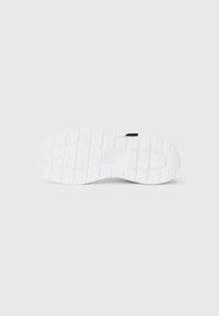 Semelle de sneaker blanche avec des motifs de grip texturés, forme plate et un subtil accent noir près du talon. Matériau en caoutchouc lisse.
