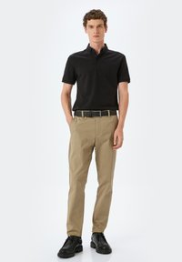 Svart pikétröja, beige byxor och svarta skor. Pikétröjan har krage och knappar; byxorna är rakskurna med ett bälte. Minimalistisk design.