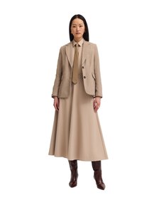 Beige taillierter Blazer über einem passenden Hemd und einem fließenden Rock. Das Outfit verfügt über bestickte Details und braune, spitz zulaufende Stiefel.